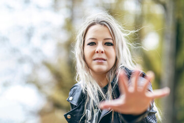 Young woman with blonde hair and leather jacket reaching hand forward outdoors in autumn light