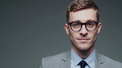 Young man in stylish suit and glasses poses confidently against a neutral background