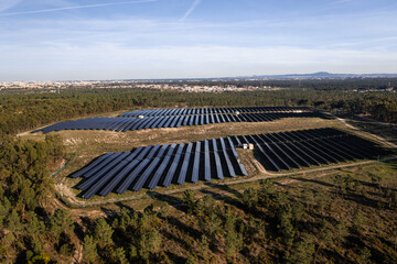 Aerial drone view of rows of solar panels in lush fields under sky generating sustainable energy with scenic townscape in background 