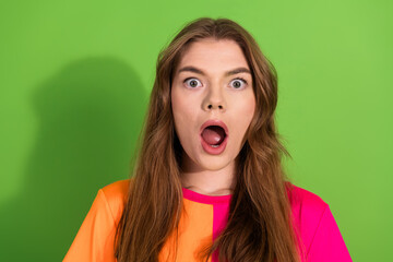 Young woman with brown hair shows shocked expression against bright green background wearing...