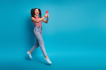 Enthusiastic young woman with striped top and ponytails holding a smartphone on a vibrant...
