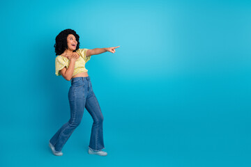 Joyful young woman pointing excitedly against a vibrant blue studio background in casual trendy attire with charming expression