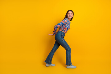 Playful young woman in stylish jeans and patterned shirt strikes a pose against a bold yellow background while showcasing casual fashion
