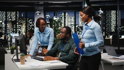 Two black workers reviewing data insights on pc in professional workspace, developing business solutions with strategy planning and performance metrics analysis for goals achievement.