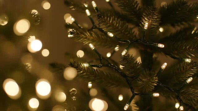 A shallow depth of field highlights pine needles adorned with small white LED string lights and surrounded by soft, out-of-focus golden bokeh orbs, evoking a festive atmosphere.