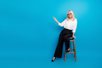 Businesswoman in elegant formalwear points with confidence while sitting on a wooden stool against...
