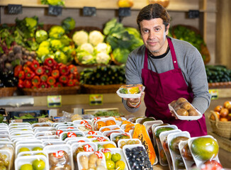 Male grocery store worker offers various packaged fruits and vegetables