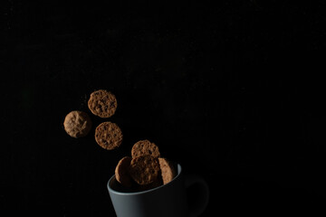 Cookies floating above a cup on dark background