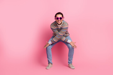 Trendy young man in patterned sweater posing against pink background with star-shaped sunglasses, showcasing fun