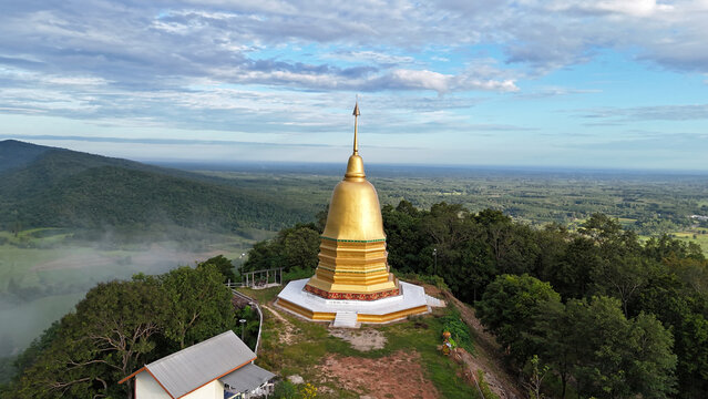 Aerial view of the golden pagoda at Wat Pa Tham Makluea, beautifully located atop a mountain in Waritchaphum, Sakon Nakhon, Thailand, shining under sunlight.