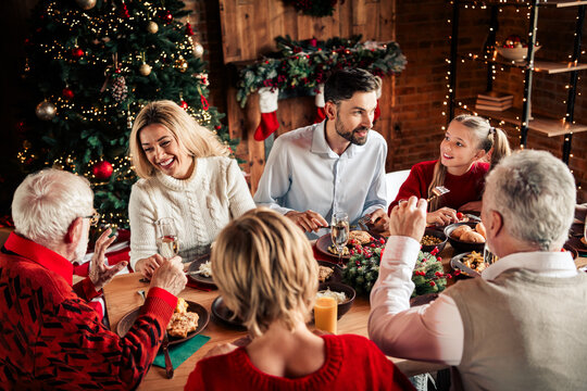 Family and friends gather for a warm Christmas dinner beside a twinkling tree in a cozy living room - Powered by Adobe