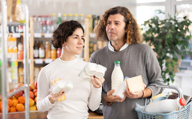 Family with various dairy products in her hands continues to make choice in grocery department of a...