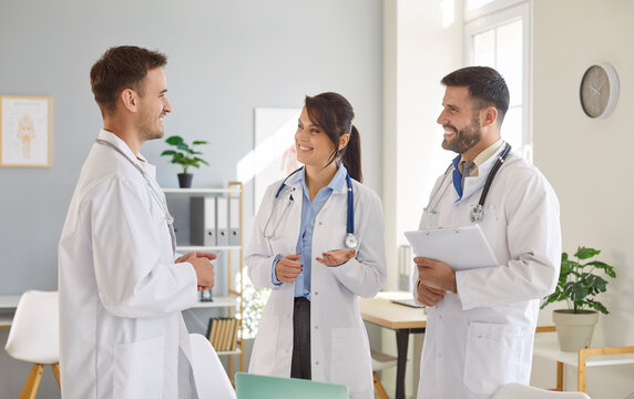 Medical staff of cheerful smiling young doctors standing on workplace in clinic discussing or planning treatment during a meeting in hospital. Healthcare, medicine and teamwork concept. - Powered by Adobe