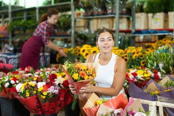 Glad young woman choosing bouquet of flowers in point of sale of plants