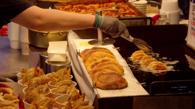 Vendor's hand flipping sweet pancakes on a frying pan next to fried dumplings