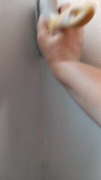 Una mano de mujer pintando la pared su casa pared de color blanco con una brocha. Video vertical 