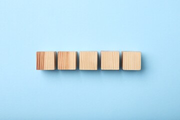 Wooden cubes on light blue background, top view