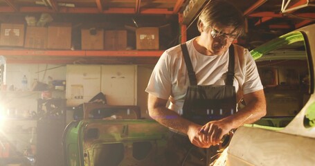 Grinding car body panel, mechanic wearing safety goggles operating grinder in workshop, copy space