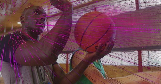 Guiding coach in sportswear showing shooting form behind youth in gym, holding ball and whistle