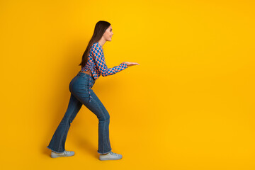 Joyful young woman in stylish jeans and patterned top leans forward with open palms toward a bold...