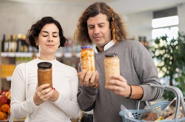 Couple choose for canned beans and lentils. European shoppers holding a jar of beans in his hands