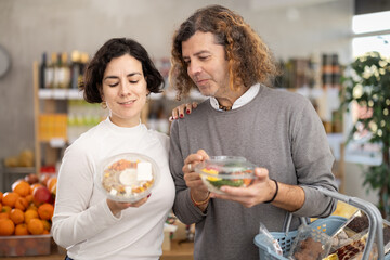 Couple choosing prepared Hawaiian food poke salad, doubt and think before buying. Client choose and...
