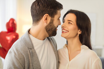Close up portrait of happy young couple standing close, gazing into each other eyes and smiling warmly. Joyful man and woman in love celebrating anniversary or Valentine Day in romantic atmosphere.