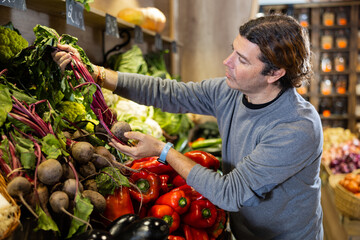 Adult man chooses beets for purchase in greengrocer shop