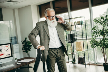 Confident senior businessman working in a modern office, managing tasks with phone in elegant...