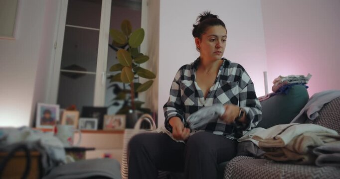 Woman folding clean laundry on sofa in evening light, focused on home organization and calm routine, simple domestic lifestyle moment expressing balance and order