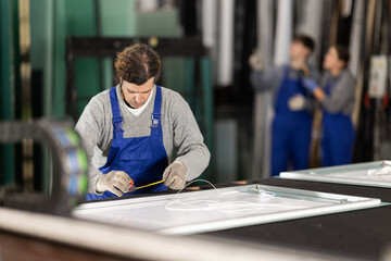Man employee works on cutting table, measuring source material with tape measure. She finds out...