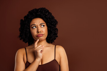 Thoughtful young woman in contemplative expression against a brown background showcasing natural...