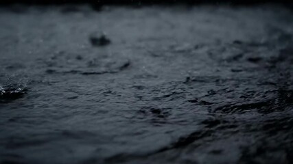 Heavy rain droplets dramatically fall onto a calm dark water surface creating intricate ripples and splashes in a moody atmosphere fluid, water, splashes - Powered by Adobe