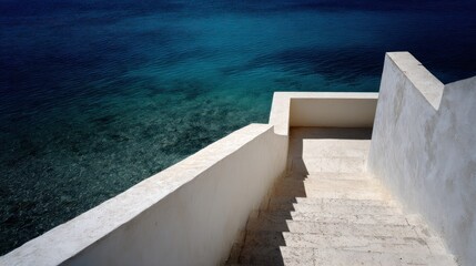 A white staircase leading down to the ocean, with a white wall on the right and a blue ocean in the background.