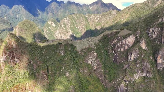Circles at a middle distance around summit of Machu Picchu during sunrise, capturing first golden light of day as it reveals different angles of the ancient Inca structures, bathing them in warm