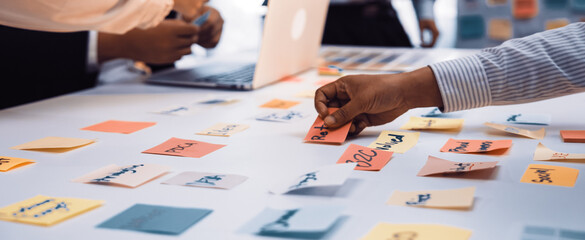 A dynamic office scene capturing a team engaged in a collaborative meeting, utilizing colorful sticky notes for brainstorming and idea generation around a laptop. SACTR