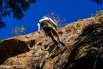 Climber descending rock face  on a belay line  with blue sky in background, room for text, shot near Calabogie in the Ottawa Valley in fall