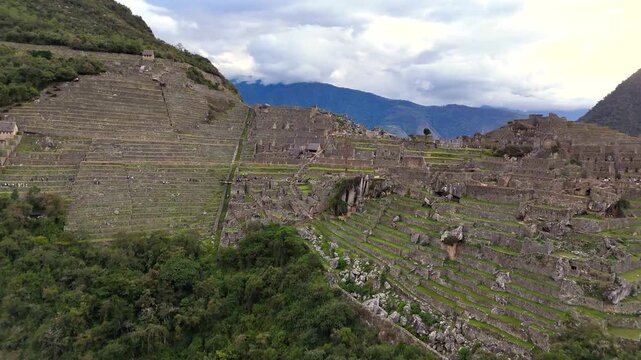 Aerial shot starts low at the bottom of the green terraces, moves forward into the heart of the Machu Picchu site, and then pans downward to reveal a central ancient stone structure from a top-down