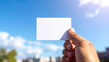 Hand Holding Blank White Business Card Against Vivid Blue Sky with Fluffy Clouds and Soft Sunlight