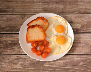 Two fried eggs, cherry tomato halves and wheat toasts on a wooden table.