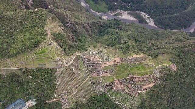 Facing down at the winding Urubamba River, pulls backward while simultaneously tilting camera upward in one fluid motion to dramatically reveal iconic Machu Picchu citadel perched atop mountain