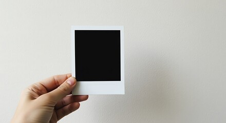 Hand holding blank black instant photo frame against textured wall polaroid