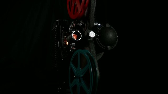 An 8mm vintage film projector operating. Film reel turning and light through lens. Panning shot on a motorized slider.