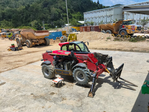 Gorontalo-Indonesia Oct 21, 2025 A red telehandler (rough terrain forklift) parked on concrete at a construction or mining yard with large articulated dump trucks and modular buildings.