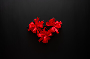 Black Friday concept with three small black gifts with red satin bows arranged as a heart on a dark background.