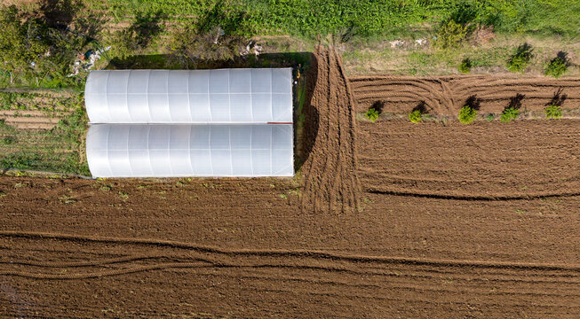 A beautiful top down aerial view of two white polytunnel greenhouses on a plot of freshly plowed brown earth on a farm - Powered by Adobe