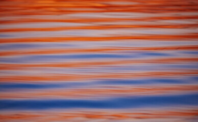 A mesmerizing background texture of calm sea surface with beautiful horizontal reflections of the orange and blue sunset sky