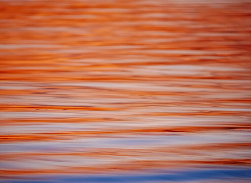 A beautiful abstract texture of warm golden sunset reflections shimmering across the gentle ripples of a calm water surface