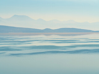 A beautiful and serene panoramic landscape of a calm lake with hazy layered mountains in the distance creating a peaceful and tranquil mood