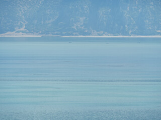 A minimalist and serene landscape of a calm blue lake with soft light and hazy mountains on the horizon a beautiful and simple nature scene